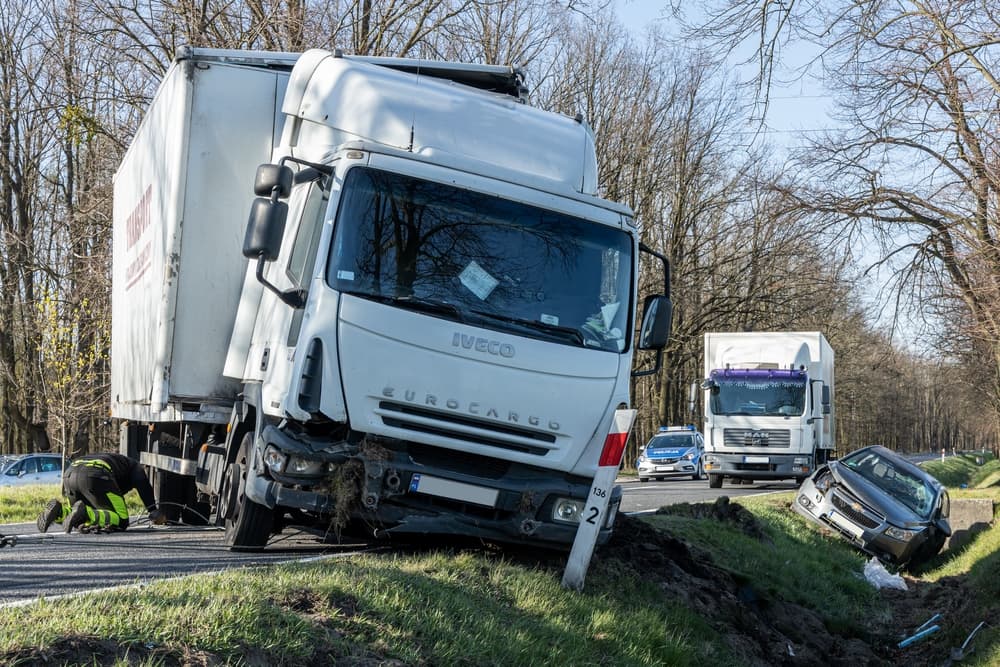 Truck collision aftermath: a wrecked passenger car lies in a ditch by the roadside.