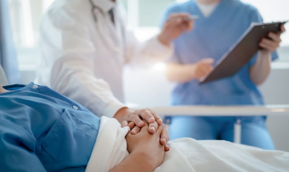 A doctor talks with a male patient during a post-surgery check-up, gently touching the patient's hand and offering reassurance.