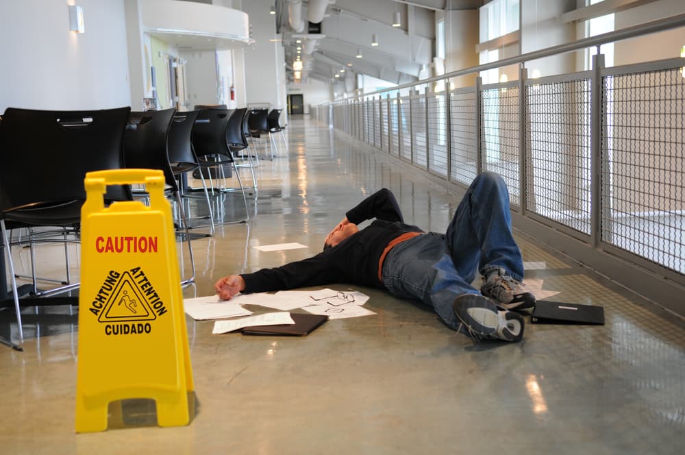 A man lies on the wet floor he slipped on despite a "Caution Wet Floor" sign, with selective focus on his head.