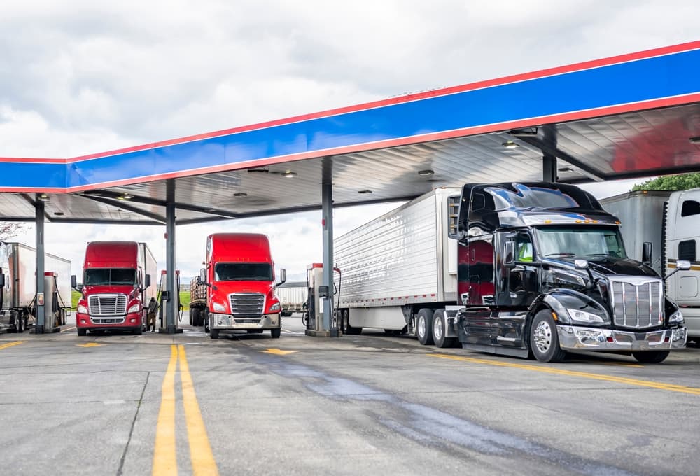 Industrial standard big rig semi trucks with trailers are parked at a fuel station, filling their tanks with diesel fuel to continue their commercial routes.






