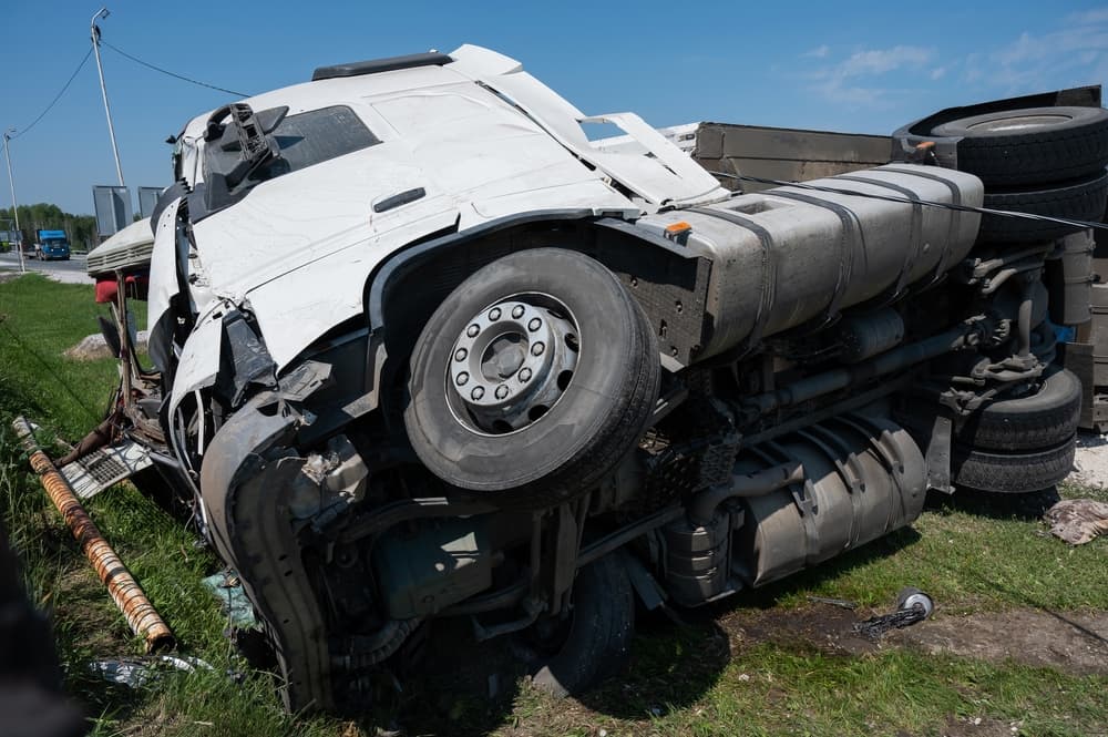 The truck lies on its side after a car accident on the highway.






