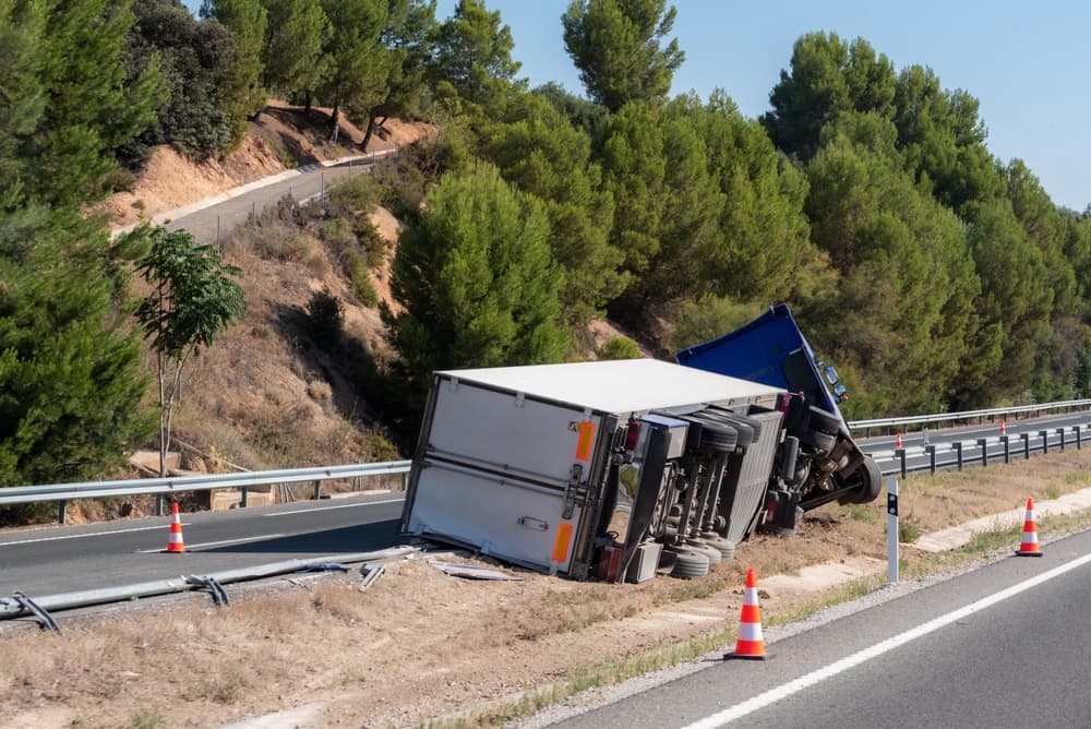 A refrigerated semi-trailer truck is overturned in the highway median near the exit.