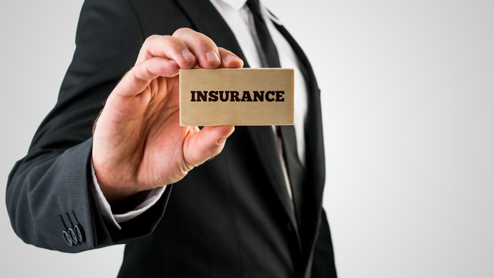 Closeup of insurance agent holding a small rectangular wooden sign saying Insurance.