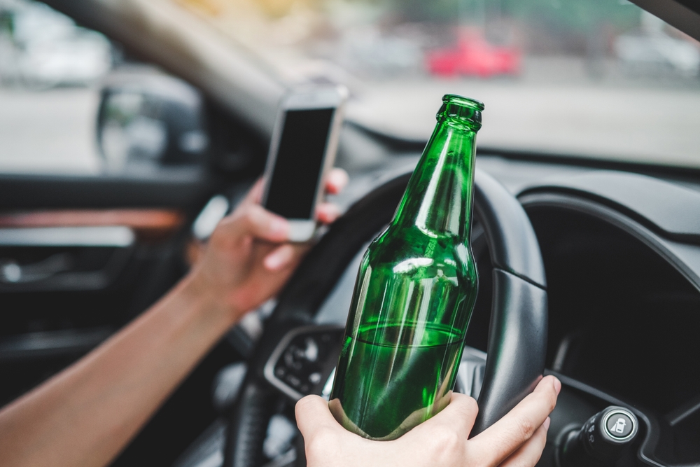 Drunk man driving a car on the road holding bottle beer Dangerous drunk driving concept