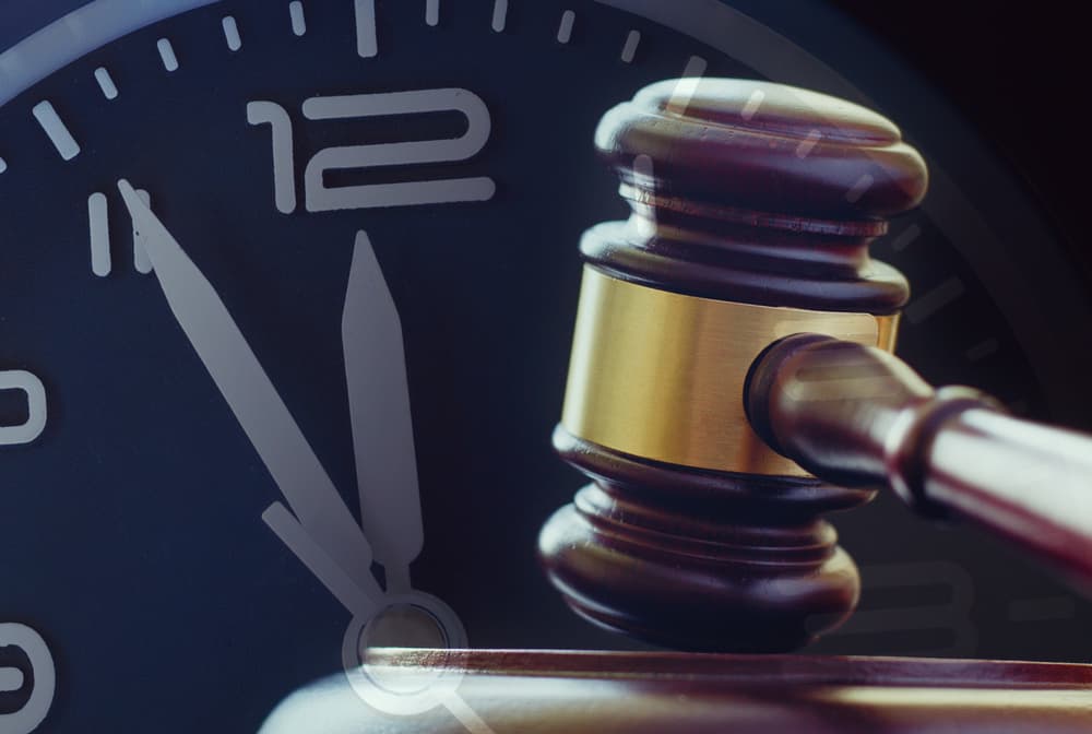 Wood and brass gavel standing upright on its base with a clock dial showing five to twelve behind in a law enforcement 